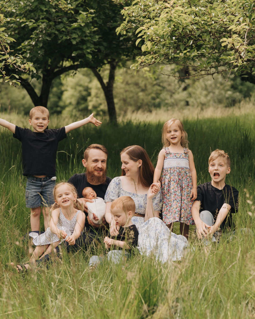 Gillian and her husband sitting in a grassy field surrounded by their six children.